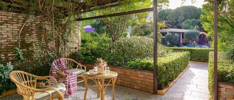 Un patio cubierto con mobiliario de mimbre, una mesa pequeña y un muro de ladrillo.