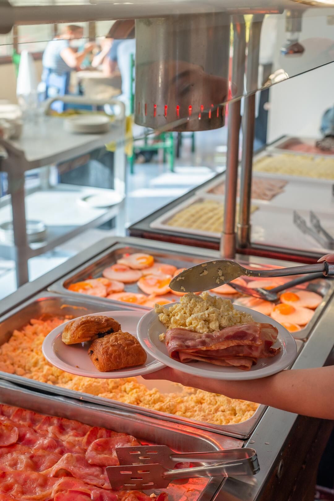 A buffet with various food options including scrambled eggs, bacon, and pastries.