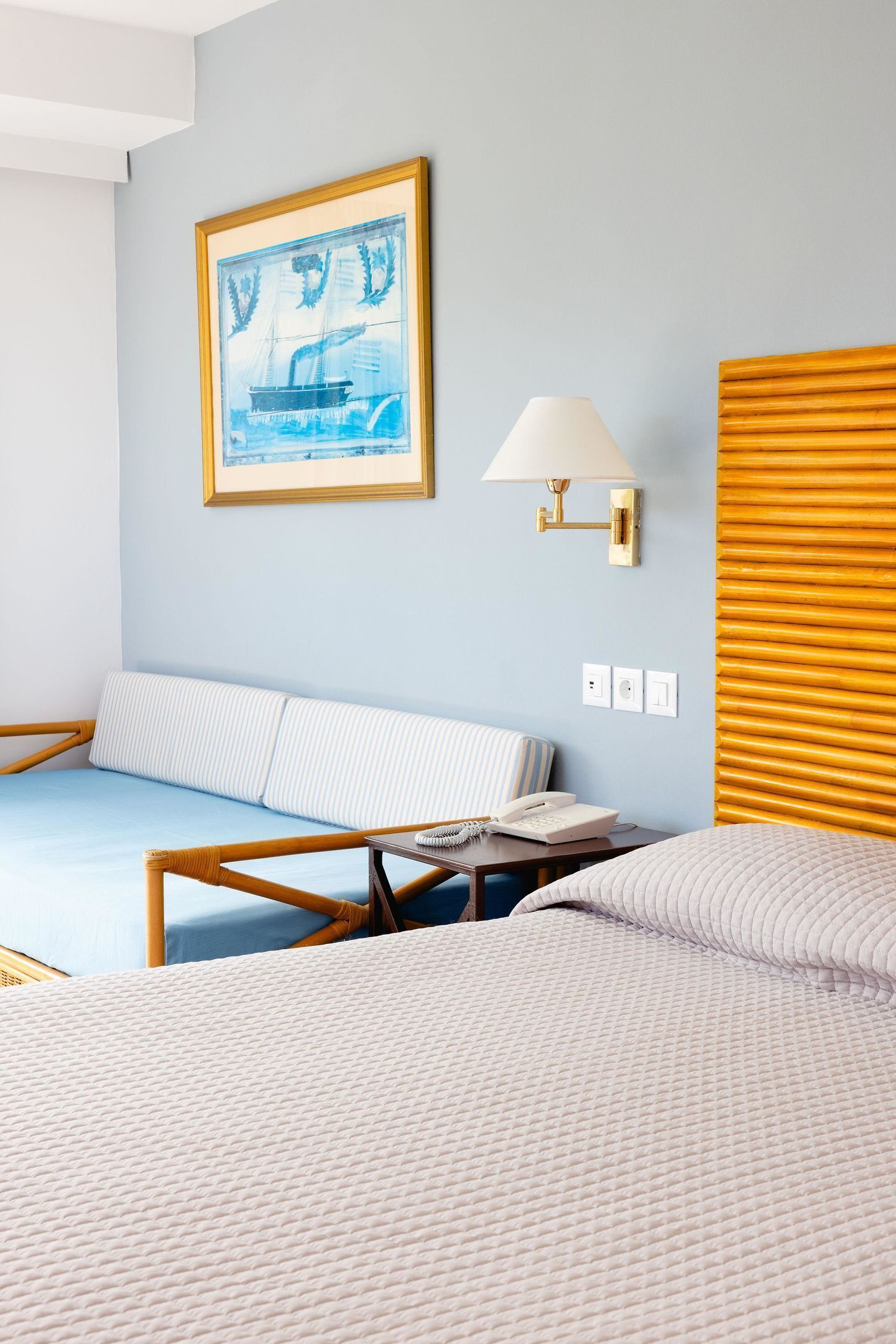 A hotel room with a bed, a sofa, a lamp, and a framed picture on the wall.