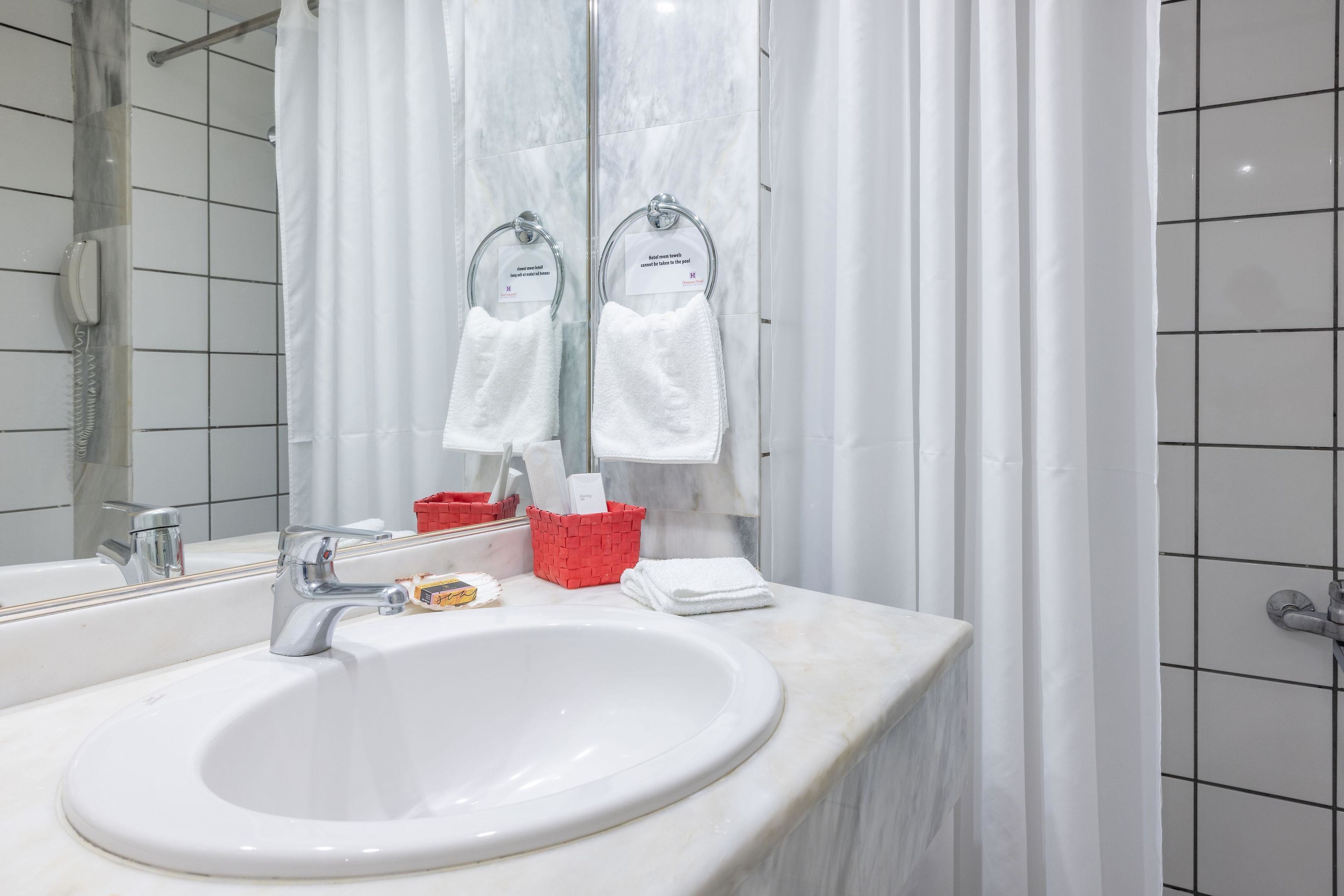 Een badkamer met een wit wastafelmeubel, een spiegel, een douchegordijn en een rode mand met toiletartikelen.