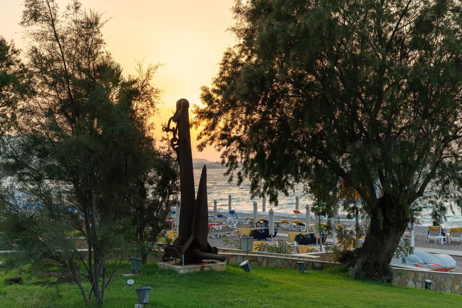 A statue in a park with a view of the sea and beach umbrellas.
