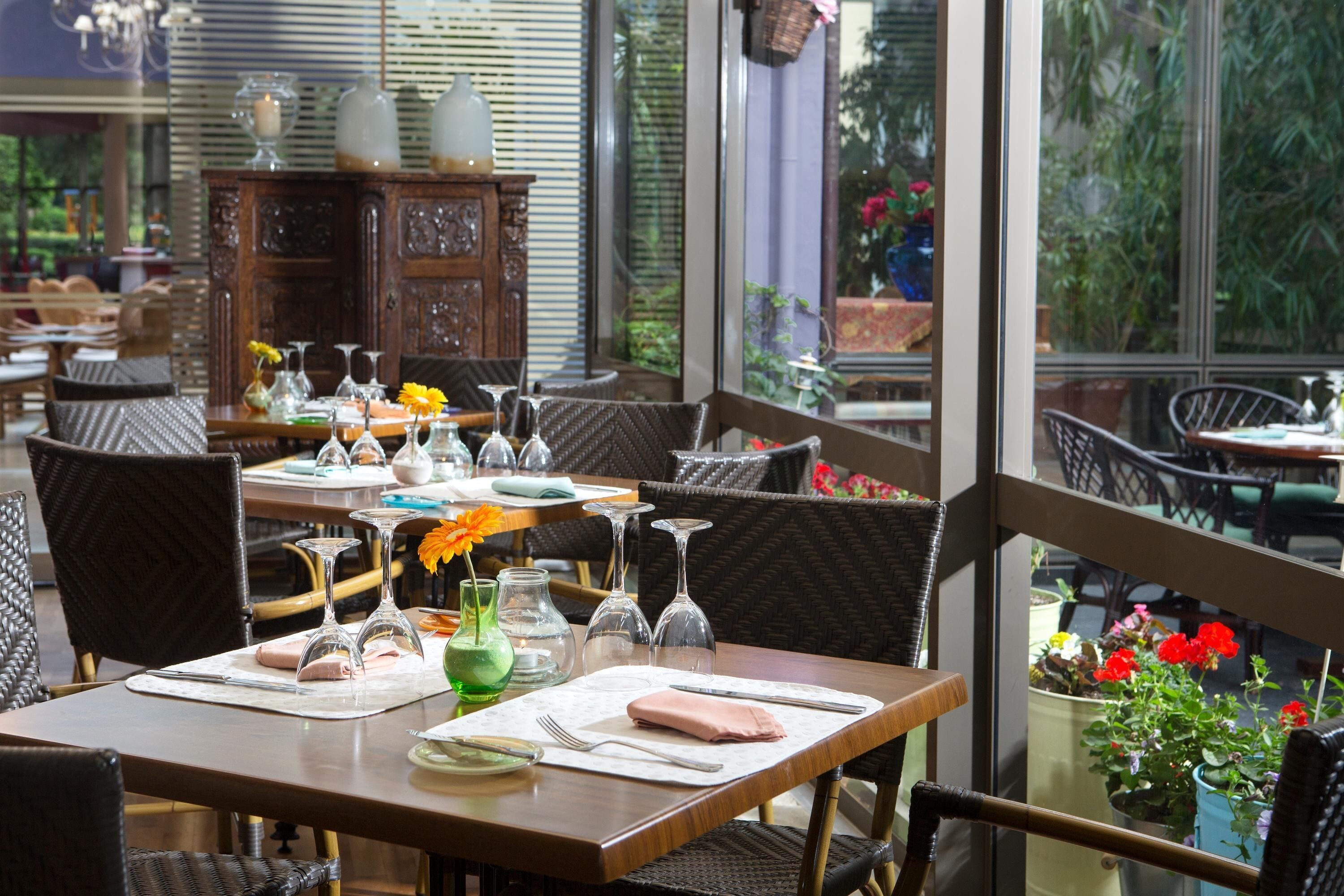 Un comedor con mesas dispuestas para dos, con sillas de mimbre y una mesa de madera.