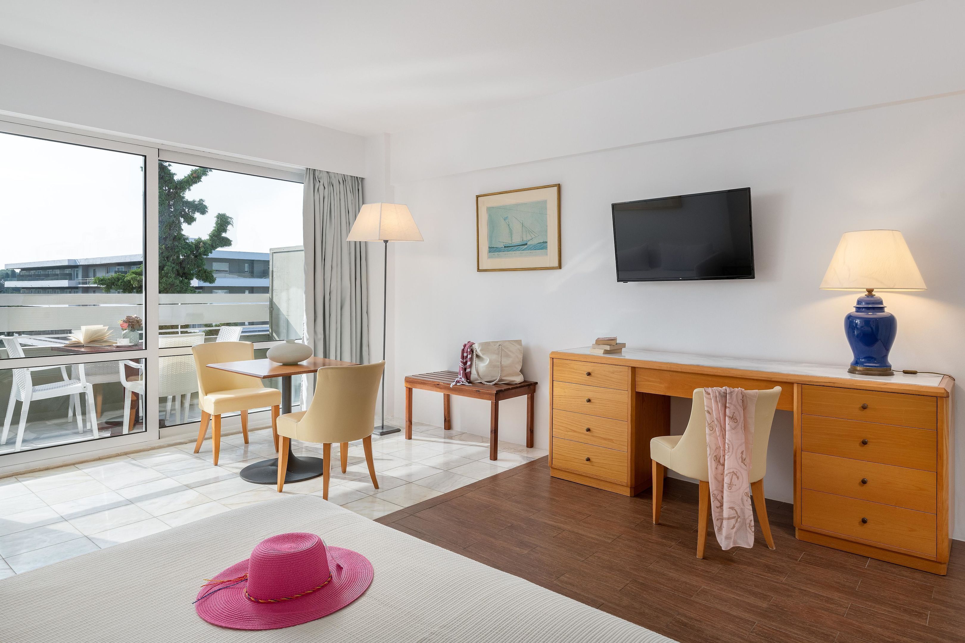 Habitación de hotel con escritorio, sillas, televisor y ventana grande con vistas a edificios.
