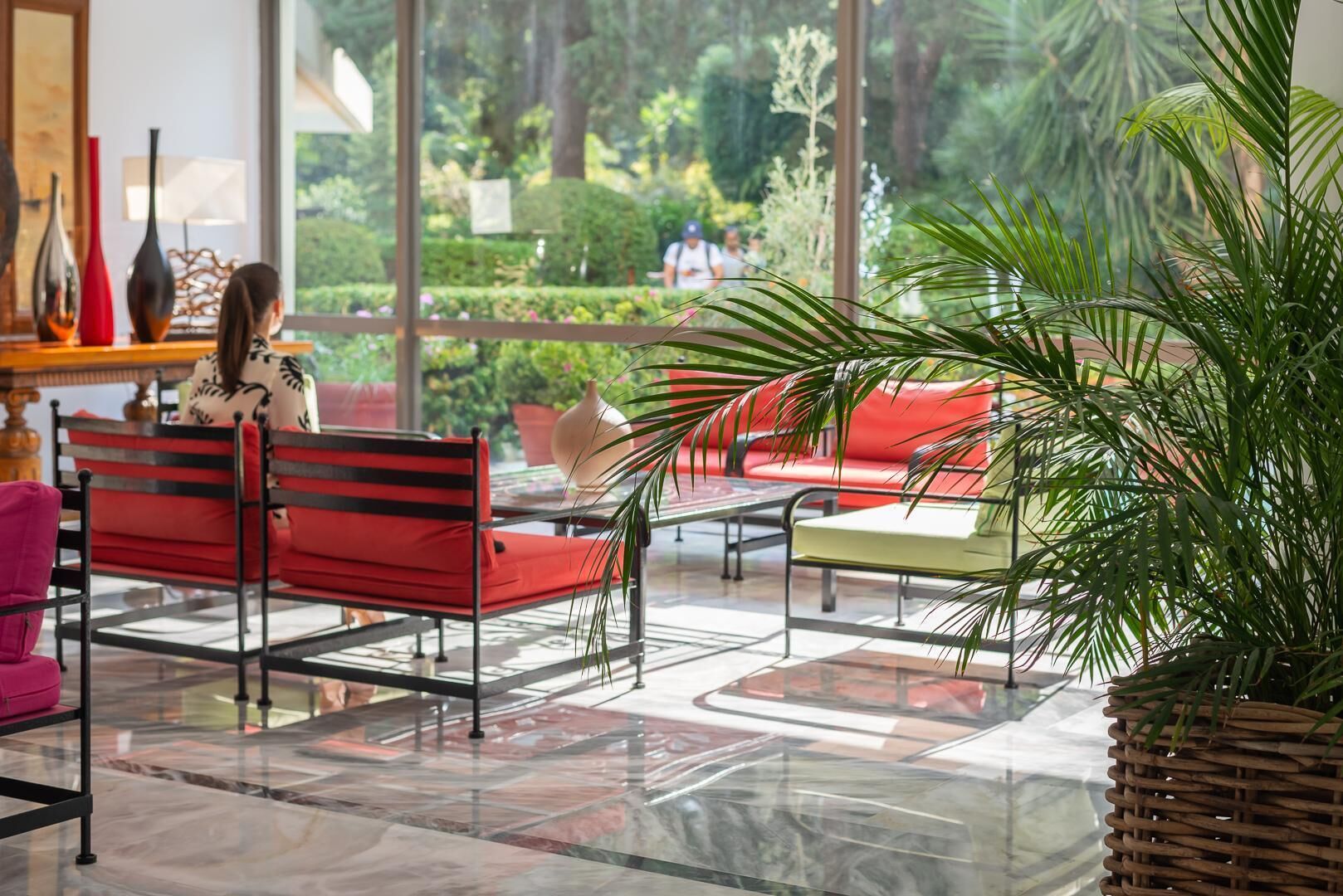 Un espacio interior amplio con piso de vidrio, asientos rojos y amarillos, y una planta grande en maceta.