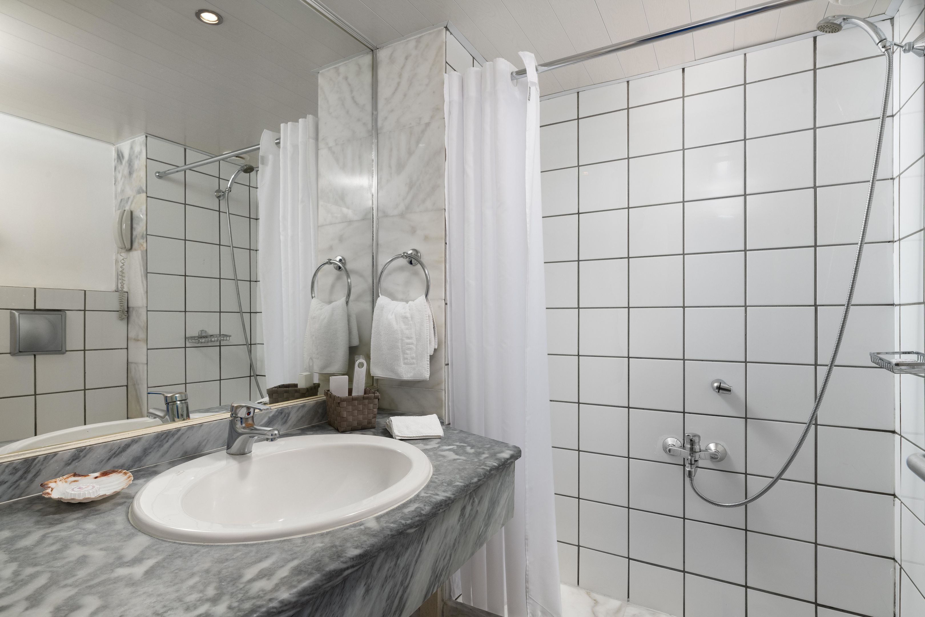 Un baño moderno con un lavabo de mármol, una ducha con puerta de cristal y un espejo con toallero.