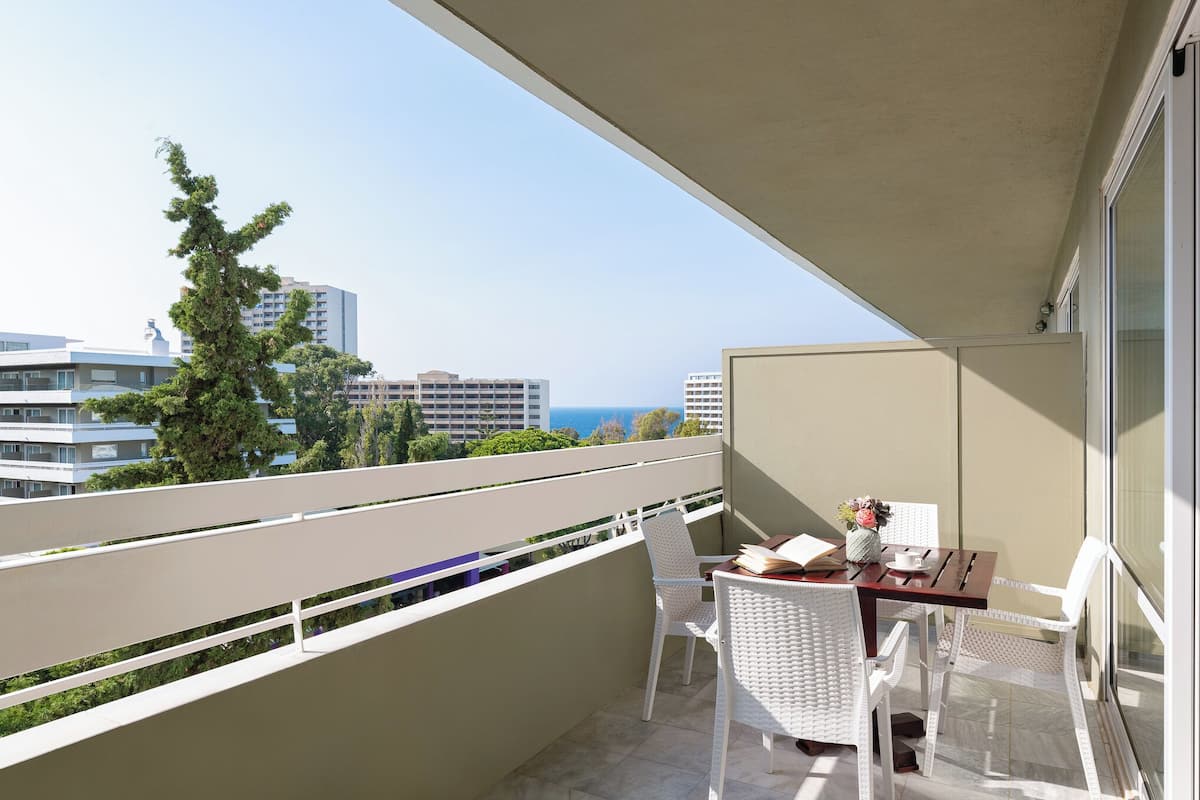 A balcony with a table and chairs, overlooking a cityscape and the sea.