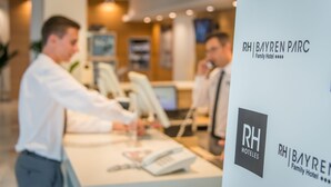 A reception desk at RH Bayren Parc with a receptionist and a guest. - Hotel RH Bayren Parc By Hoteles RH (Gandia)
