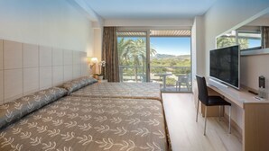 A hotel room with two beds, a TV, a desk, and a balcony with a view of palm trees and hills. - Hotel RH Bayren Parc By Hoteles RH (Gandia)