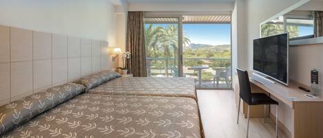 A hotel room with two beds, a TV, a desk, and a balcony with a view of palm trees and hills.