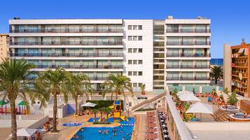 A hotel with multiple balconies, a swimming pool, and sun loungers.