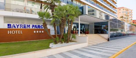 A hotel entrance with a modern facade, palm trees, and a clear view of the building's exterior.