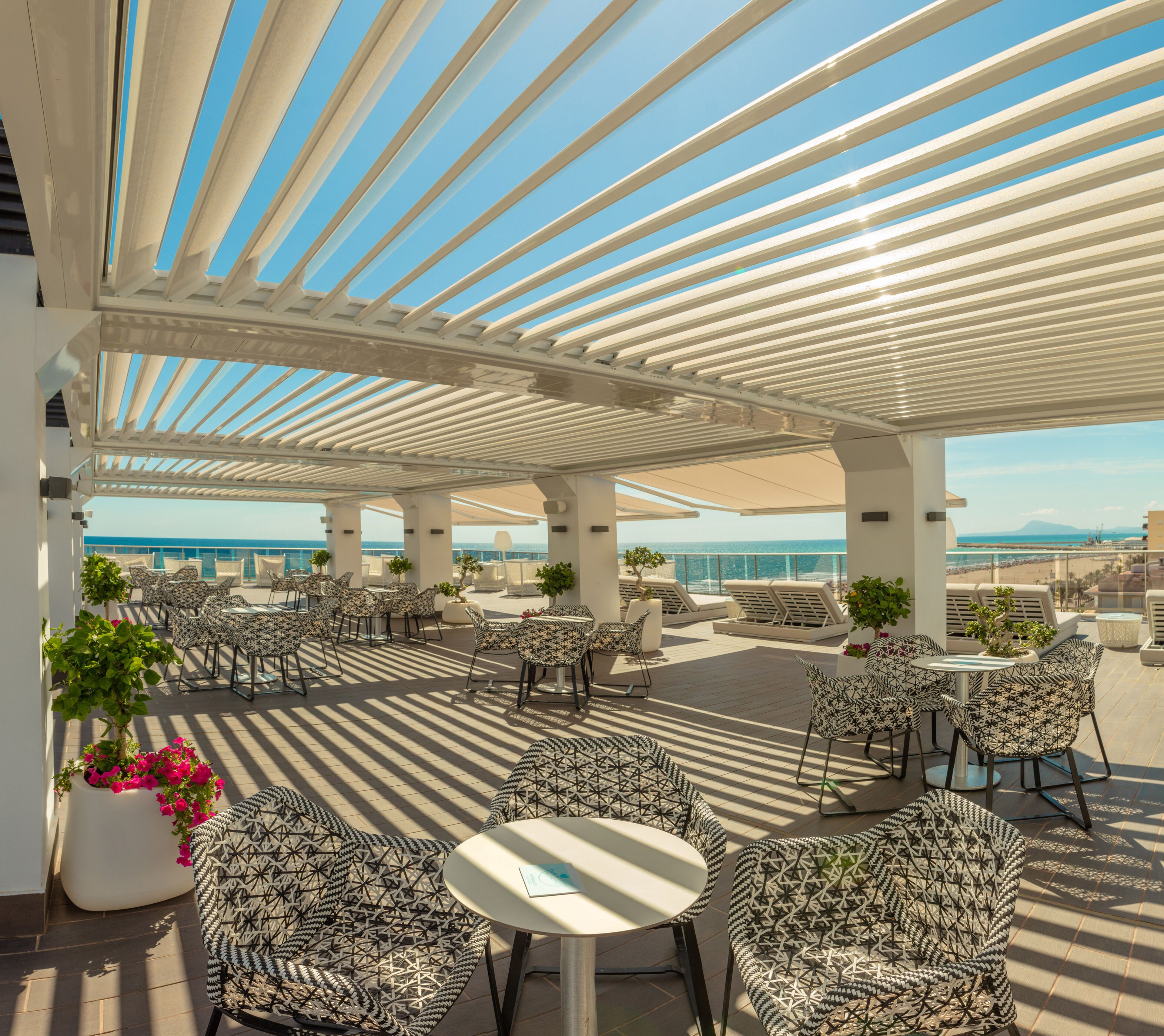 Una terraza al aire libre con asientos estampados, una pérgola y vistas al mar.