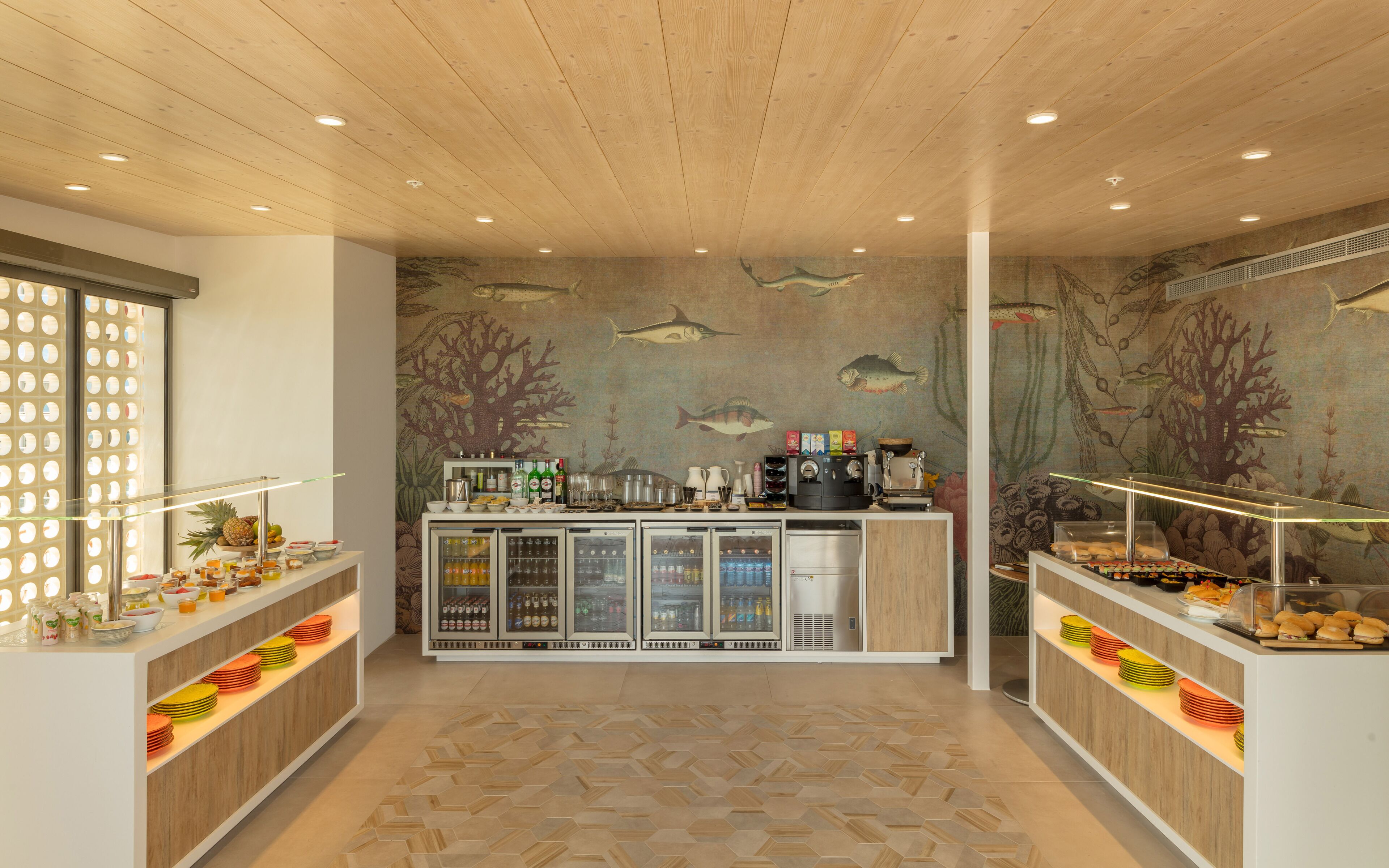 Een ontbijtbuffet met wanddecoratie met zeeschepsmotieven, een koffieapparaat en diverse ontbijtartikelen.