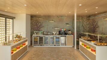 Een ontbijtbuffet met wanddecoratie met zeeschepsmotieven, een koffieapparaat en diverse ontbijtartikelen.