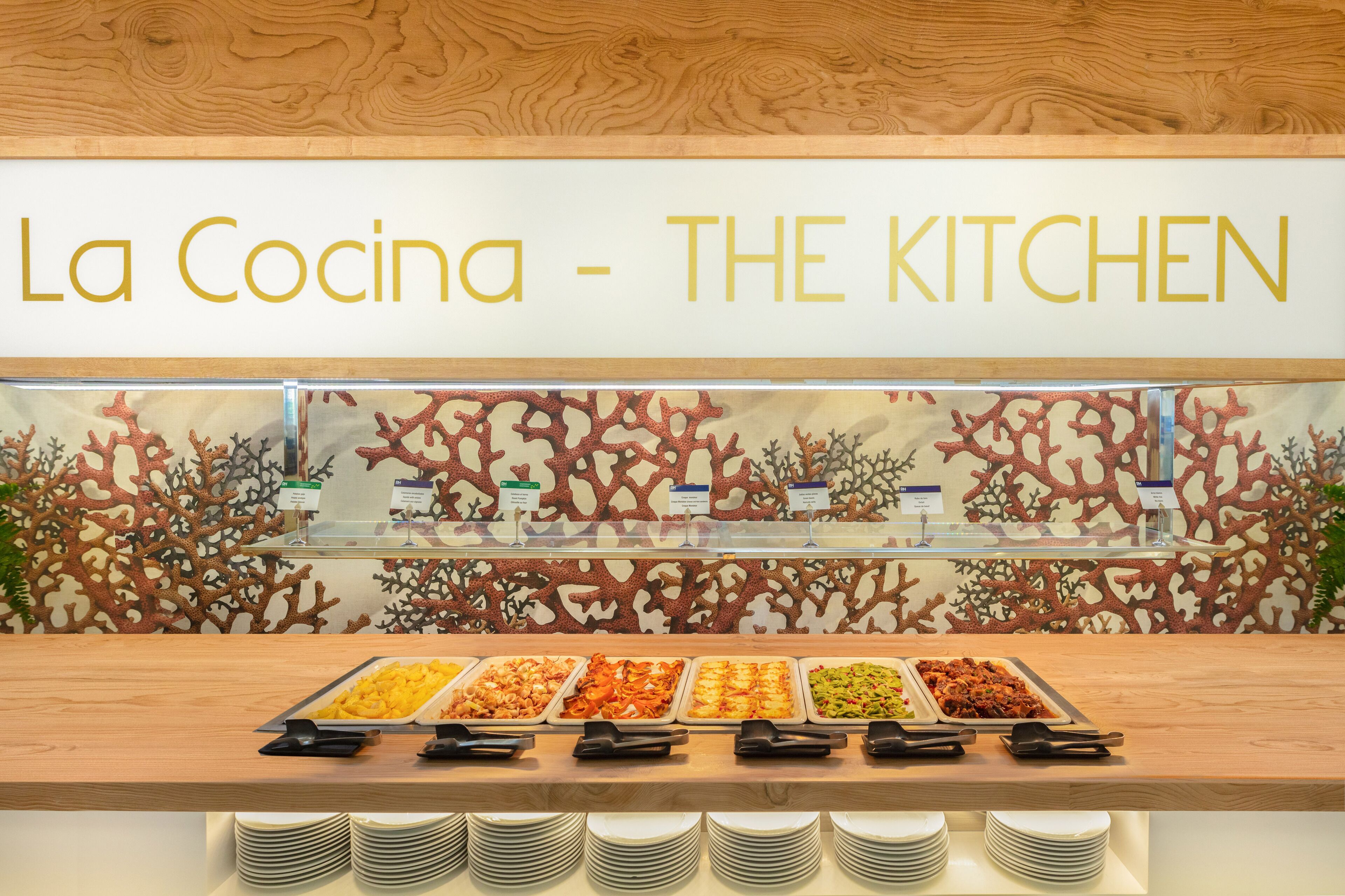 En buffetbod med forskellige madmuligheder og et skilt der siger "La Cocina - THE KITCHEN".