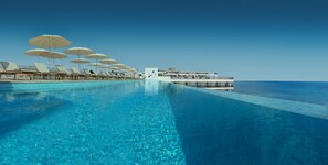 A poolside area with lounge chairs and umbrellas, a clear blue pool, and a building with a balcony overlooking the sea. - RH Bayren Hotel & Spa By Hoteles RH (Gandia)