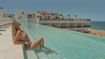 Ein Poolbereich mit Liegestühlen, einem Pool und Blick auf Strand und Meer.