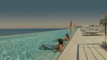 Uma piscina com água cristalina, cadeiras de descanso próximas e vista para o oceano.