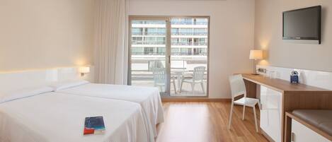 A hotel room with two beds, a desk, a chair, a TV, and a balcony with a view of other buildings.