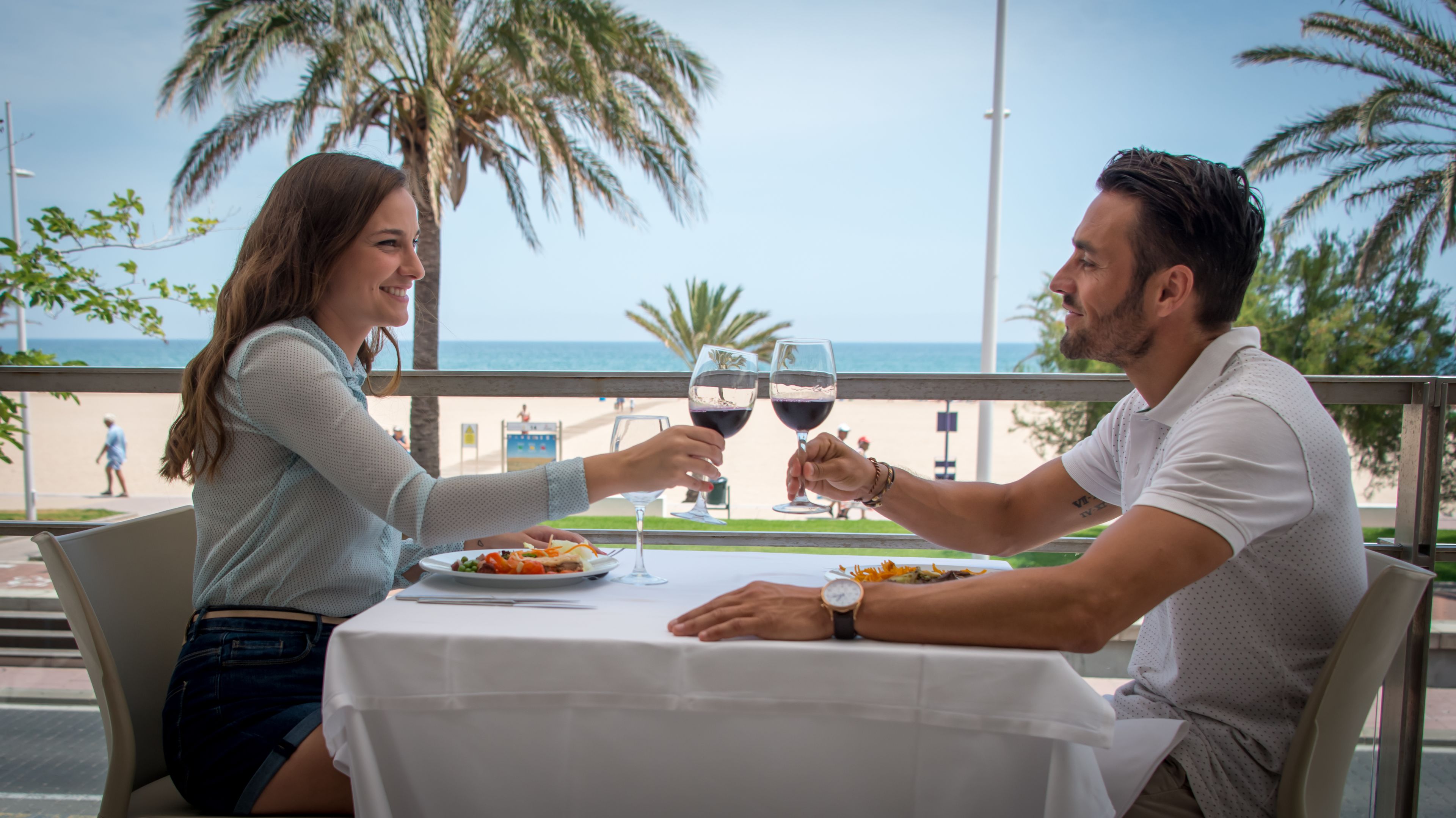 A couple dining at a table with a view of the beach and palm trees.
