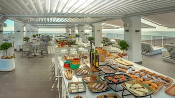 A rooftop dining area with a variety of food and drinks, outdoor seating, and potted plants.