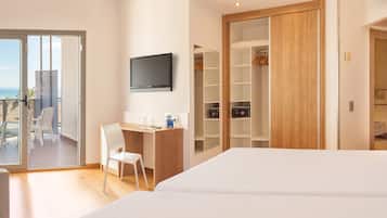 Habitación de hotel con cama, escritorio, silla, televisor y armario. Tiene un balcón con vista a la playa.