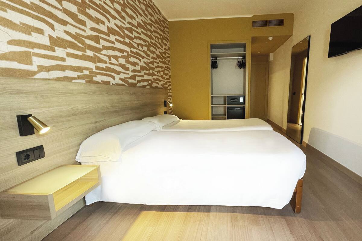 Una habitación de hotel con una cama, un espejo, un televisor y un armario.