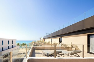 A rooftop terrace with sun loungers, a glass balustrade, and a view of the sea.