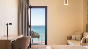 Habitación de hotel con cama, escritorio, silla y balcón con vistas al mar.