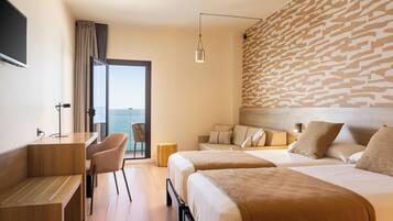 Ein Hotelzimmer mit zwei Betten, einem Schreibtisch und einem Stuhl. Ein großes Fenster bietet Blick aufs Meer.