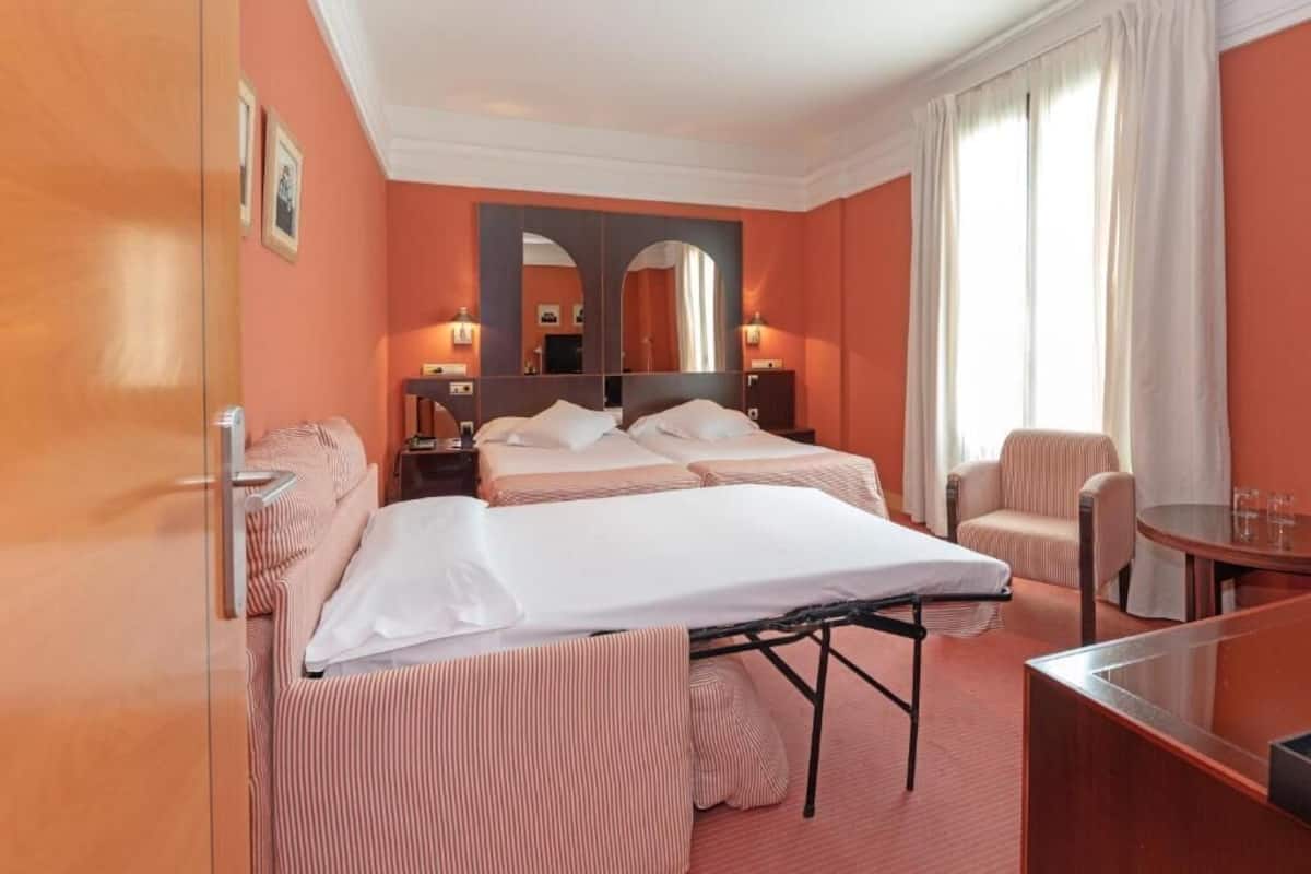 Une chambre d’hôtel avec deux lits, un coin salon comprenant une chaise, une petite table et un miroir.