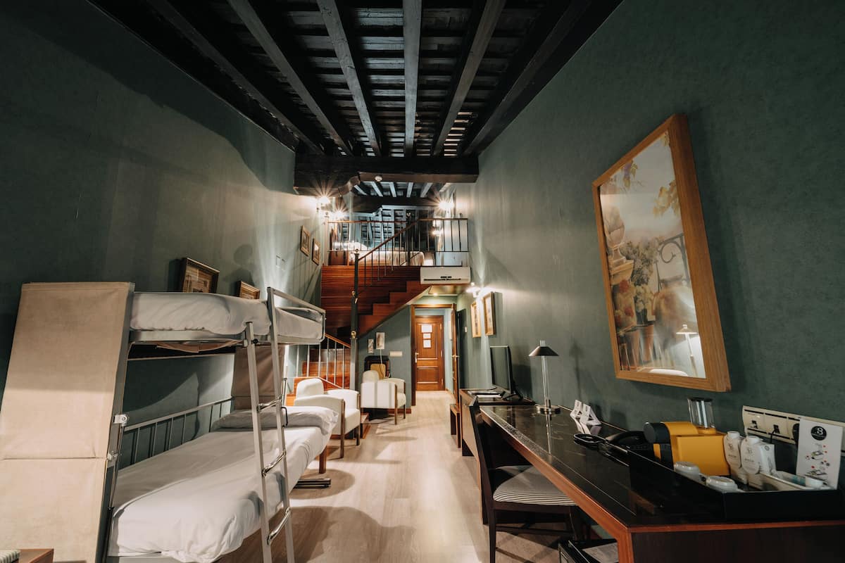 Une chambre d’hôtel avec des lits superposés, un bureau, une chaise, une machine à café et un escalier menant à un étage supérieur.