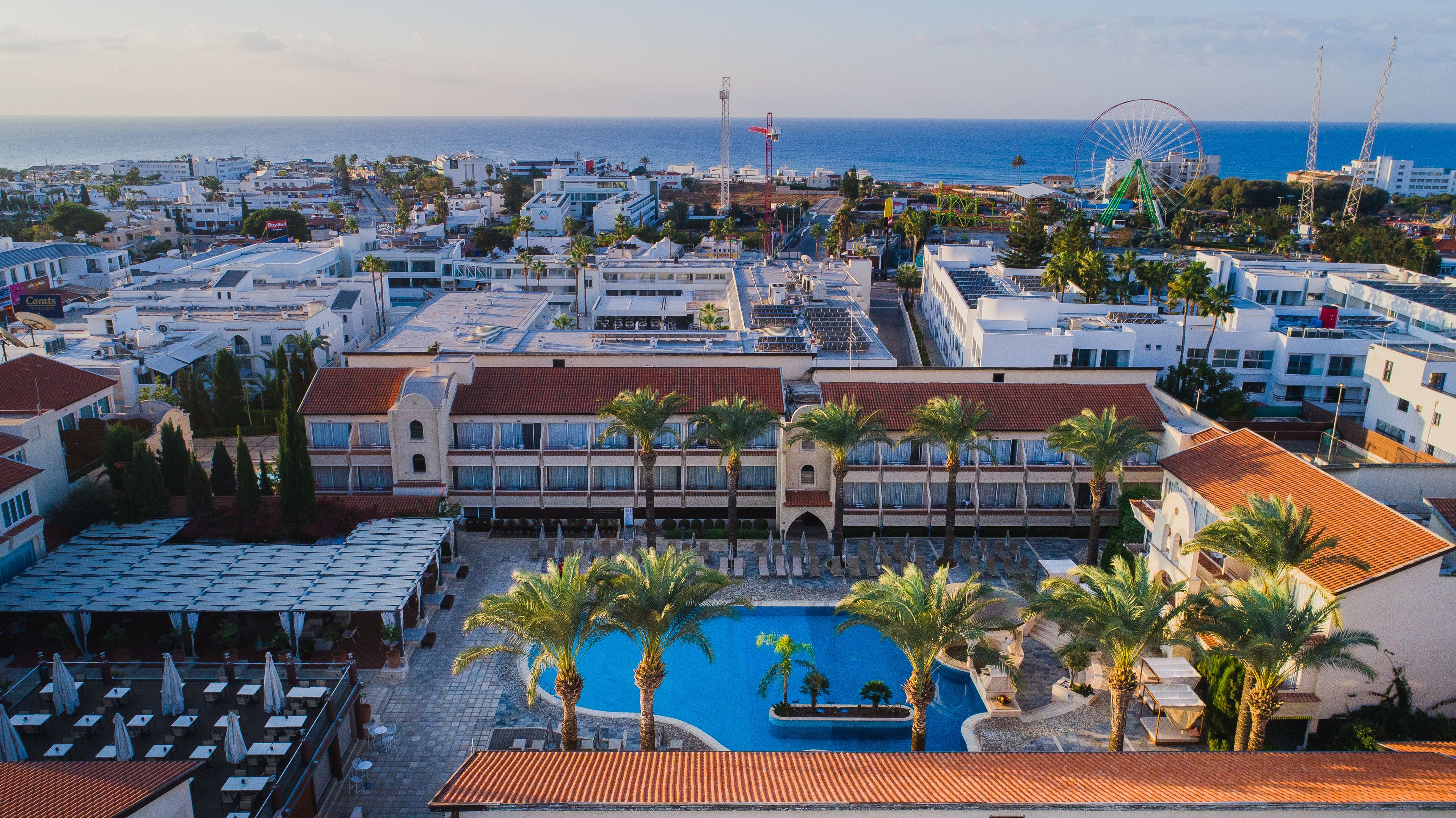 A resort with a swimming pool, multiple buildings, and a view of the sea.