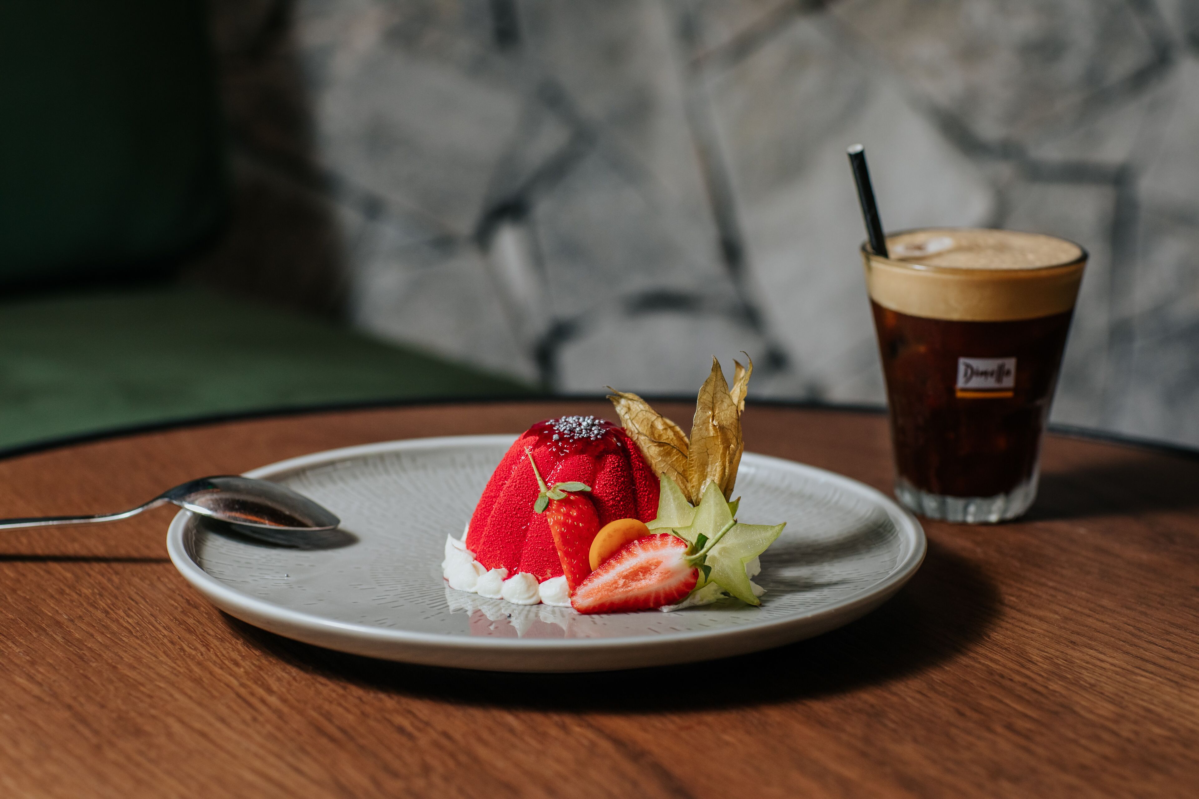 Un dessert su un piatto con un cucchiaio, una bevanda con una cannuccia e un cuscino verde sullo sfondo.