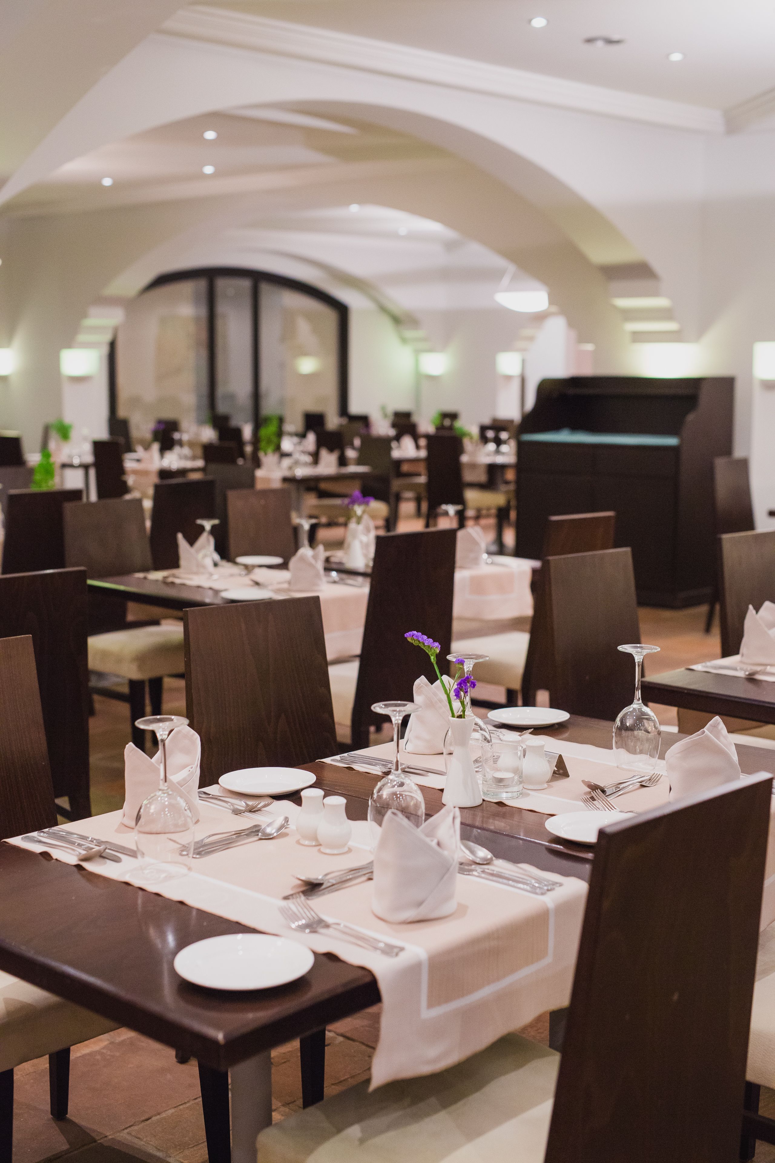 Ein Restaurant mit gedeckten Tischen, weißen Tischdecken, ordentlich drapiertem Besteck und dekorativen Vasen.