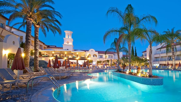A resort pool area with lounge chairs, umbrellas, and palm trees.