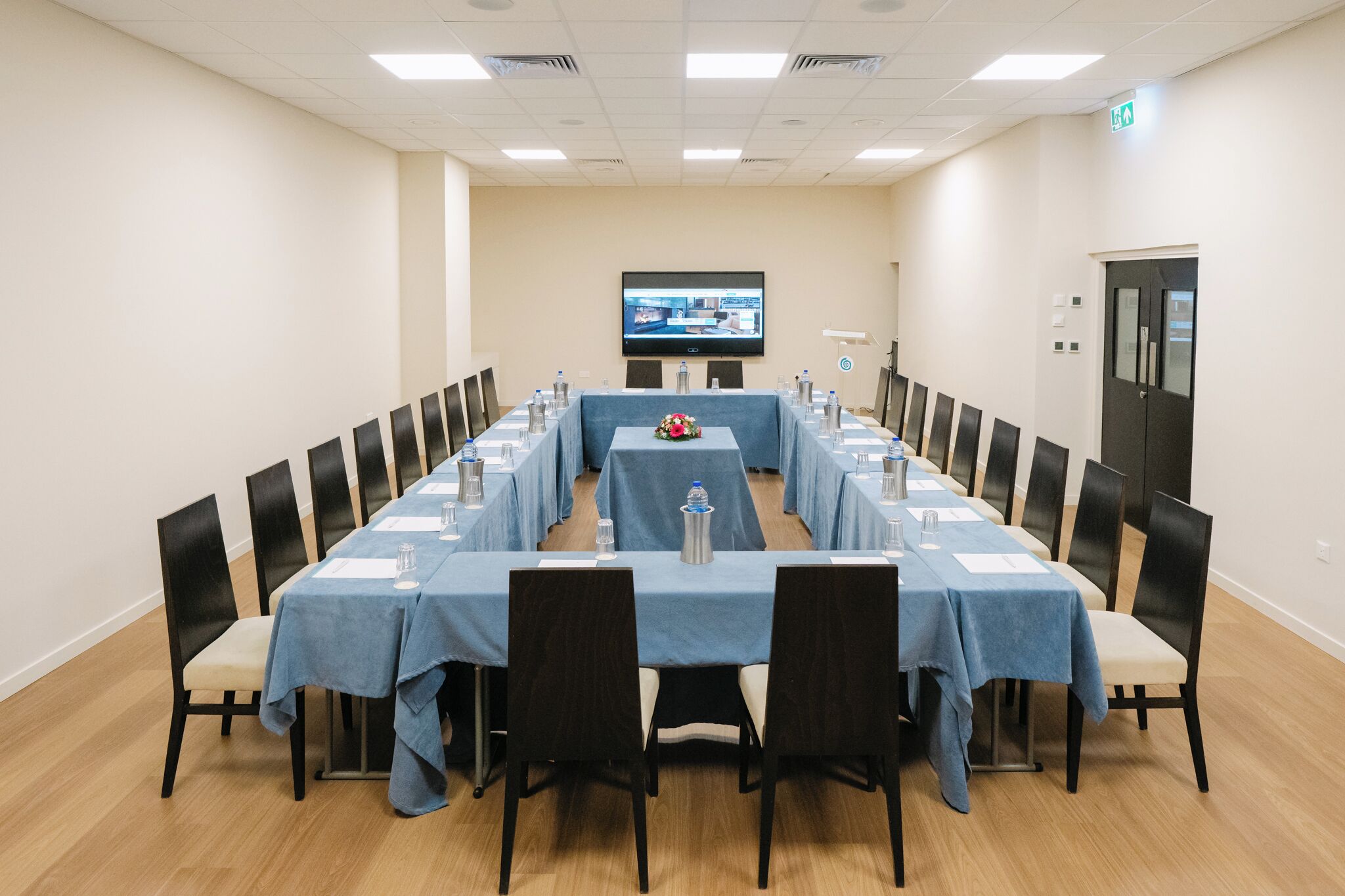 A conference room with a long table, chairs, a TV screen, and a door.