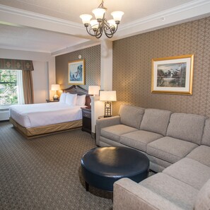 A hotel room with a bed, a sofa, a small table, a lamp, and a painting on the wall.