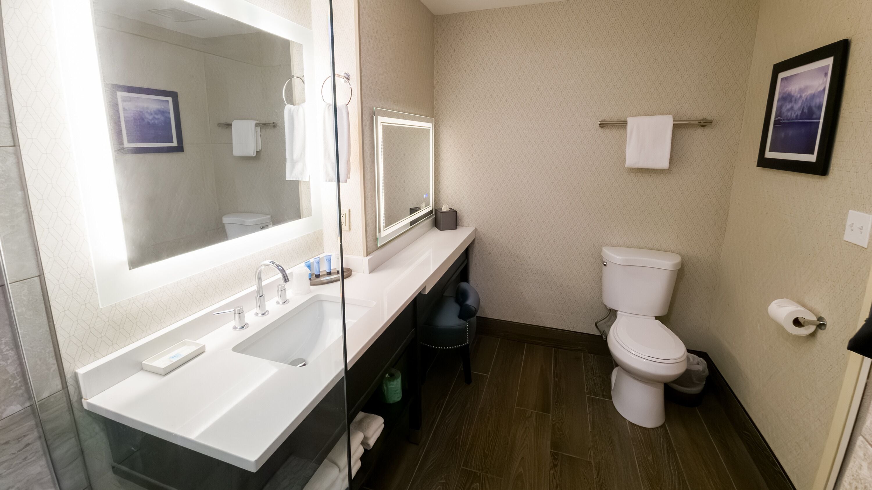 A modern bathroom with a large mirror, a sink, a toilet, and a trash bin.