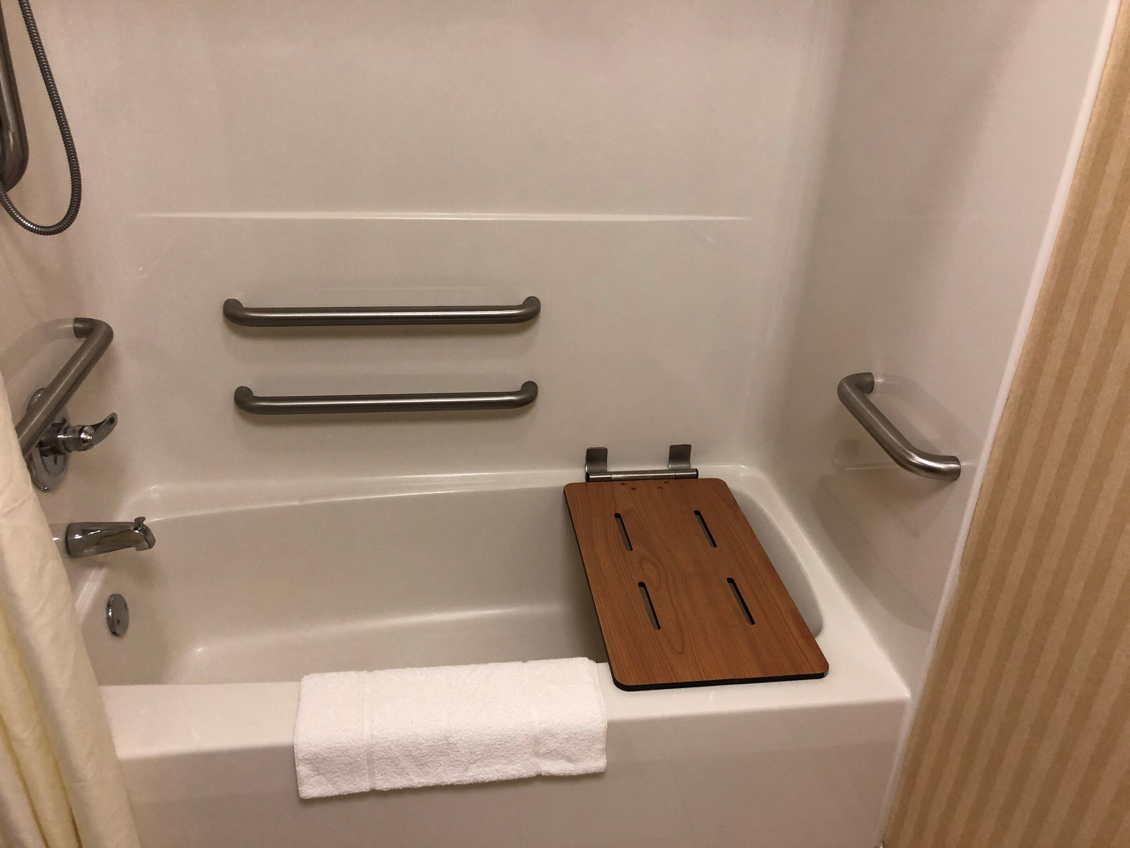 A bathtub with grab bars, a wooden tray, and a white towel.