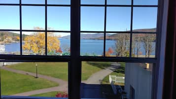A view through a window with a clear sky, a lake, and autumn-colored trees.