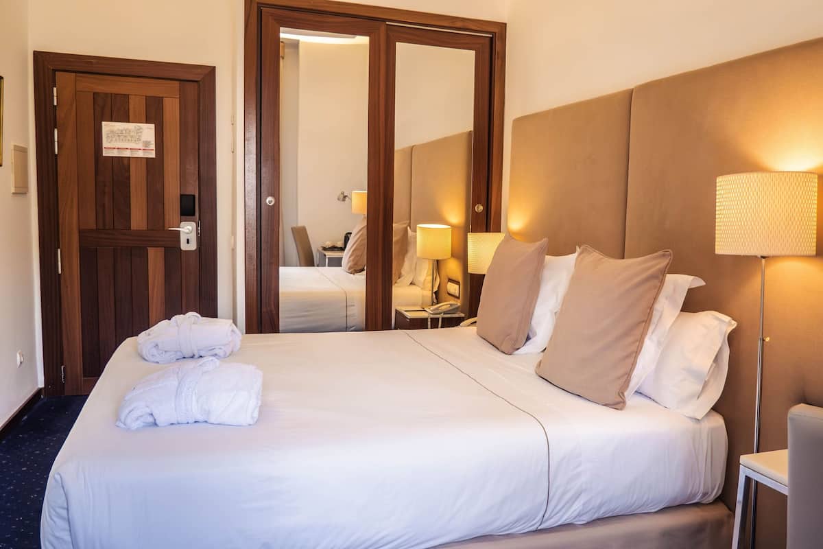 A hotel room with a large bed, a bedside lamp, a chair, and a desk with a lamp.