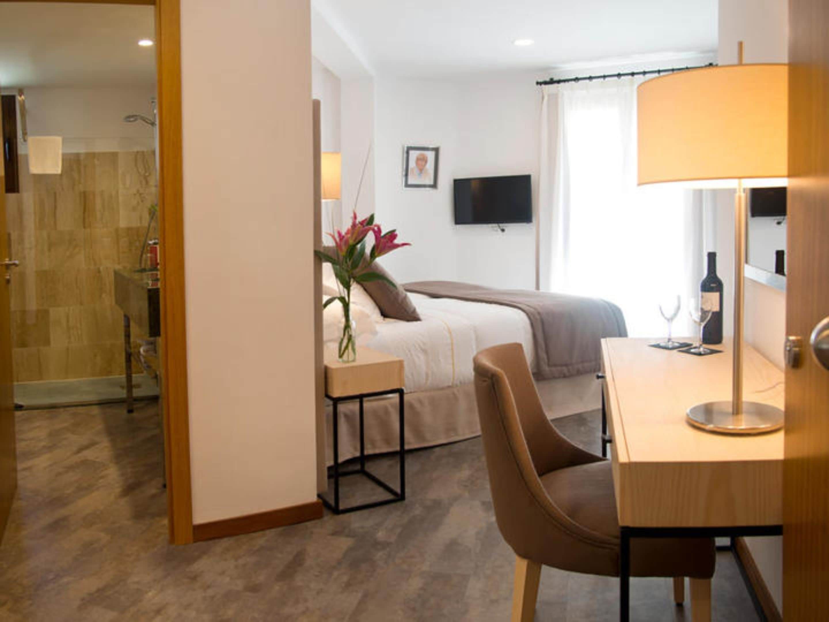 Habitación de hotel con cama, escritorio con lámpara, televisor y zona de ducha.