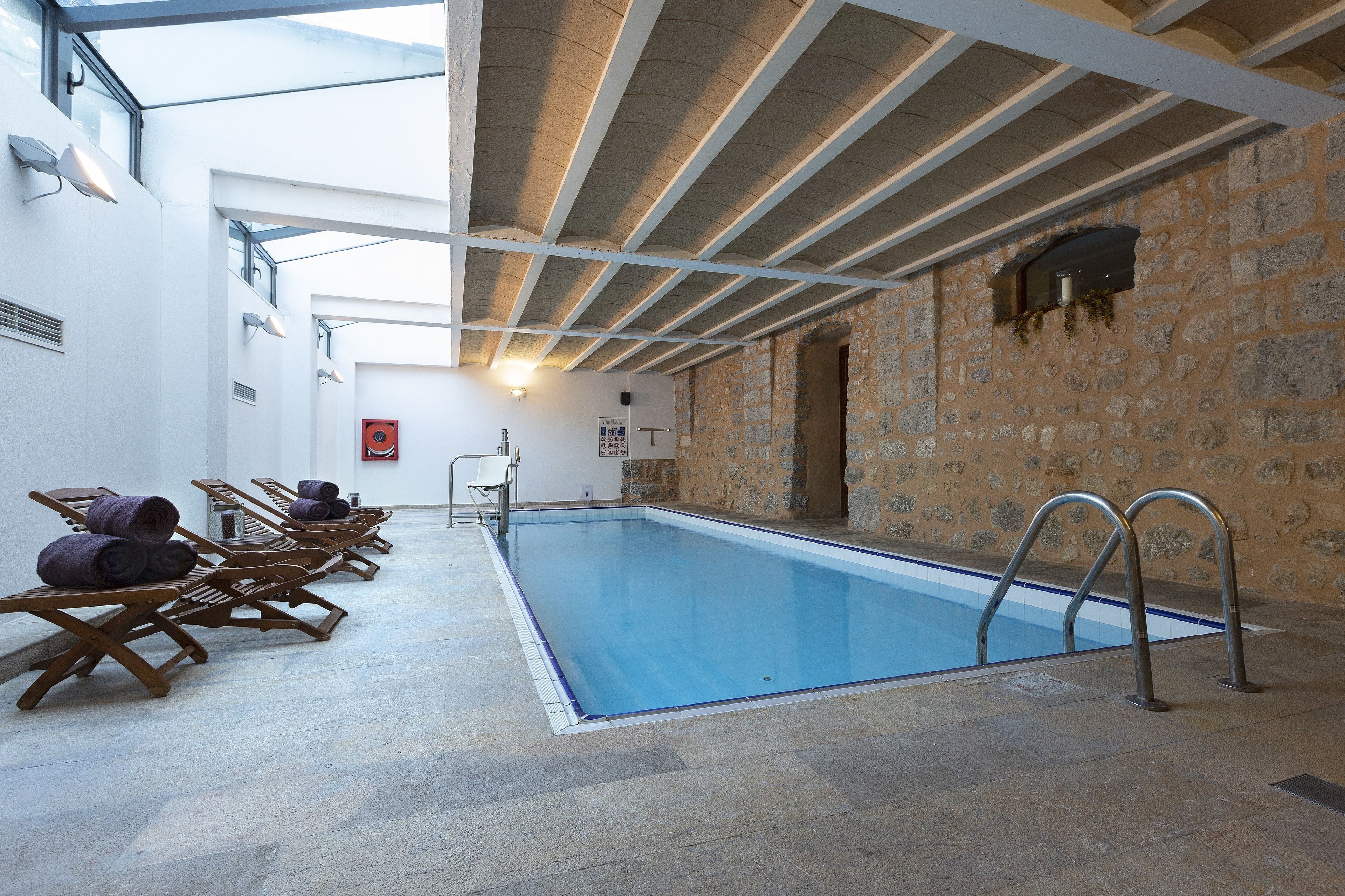 A swimming pool with wooden loungers and a stone wall.