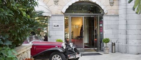 A vintage car parked in front of a building with a stone facade and an arched entrance.