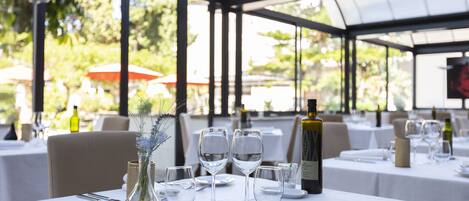 A restaurant with tables set for dining, clear glassware, and a bottle of wine on the table.