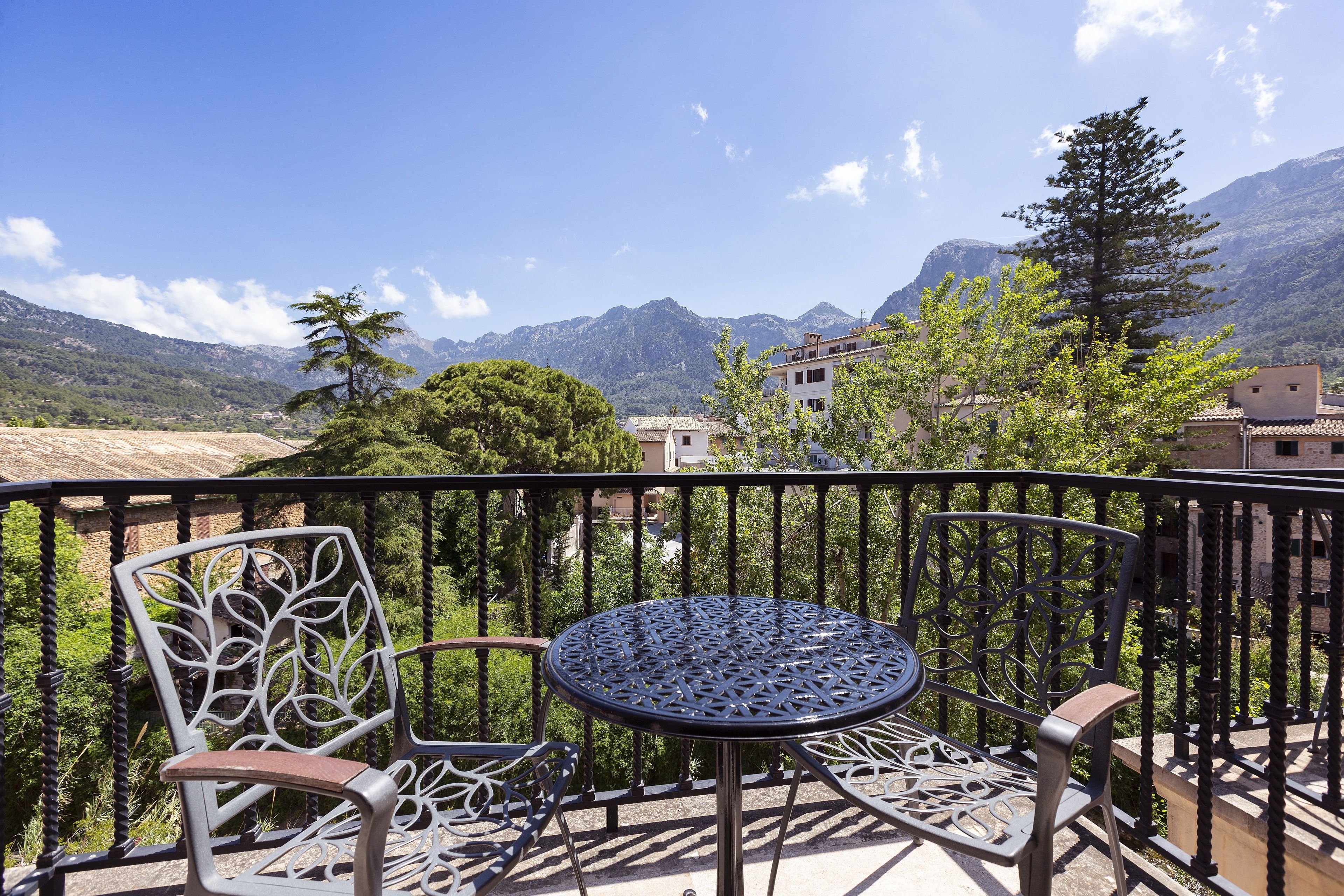 A balcony with a metal table and chairs, overlooking a mountainous landscape with buildings in the background.