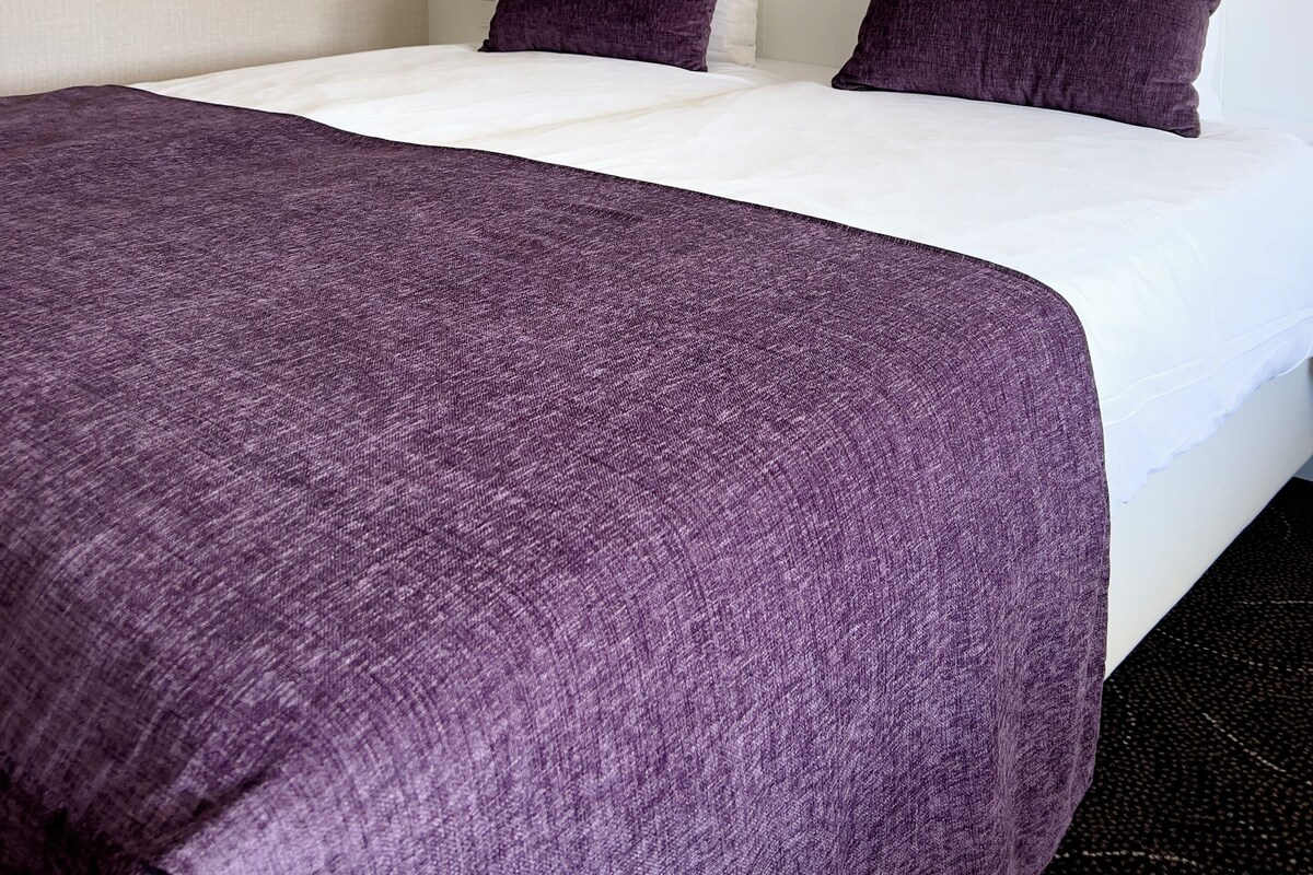 Ein Hotelzimmer mit einem großen Bett, einem weißen Kopfteil und zwei violetten Kissen.