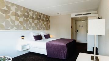 Une chambre d’hôtel avec un lit, une table de chevet, une lampe et un mur orné d’un motif géométrique.