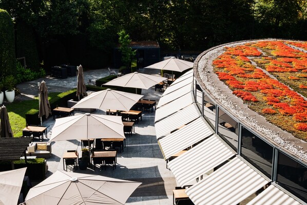 An outdoor seating area with tables and umbrellas, surrounded by a garden with red flowers.